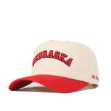 Introducing the Right Side Up Nebraska Hat - Classic by No Rivals: this beige baseball cap features a striking red brim and "NEBRASKA" embroidered in bold red letters across the front. Made from high-quality cotton, this snapback hat showcases an embroidered logo along with subtle red text on the side.