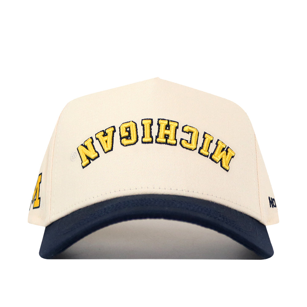 The No Rivals Michigan Wolverines | Upside Down Michigan Hat - Classic features a white cotton design with a navy blue brim, bold yellow MICHIGAN text embroidered upside down on the front, and a classic snap back closure.