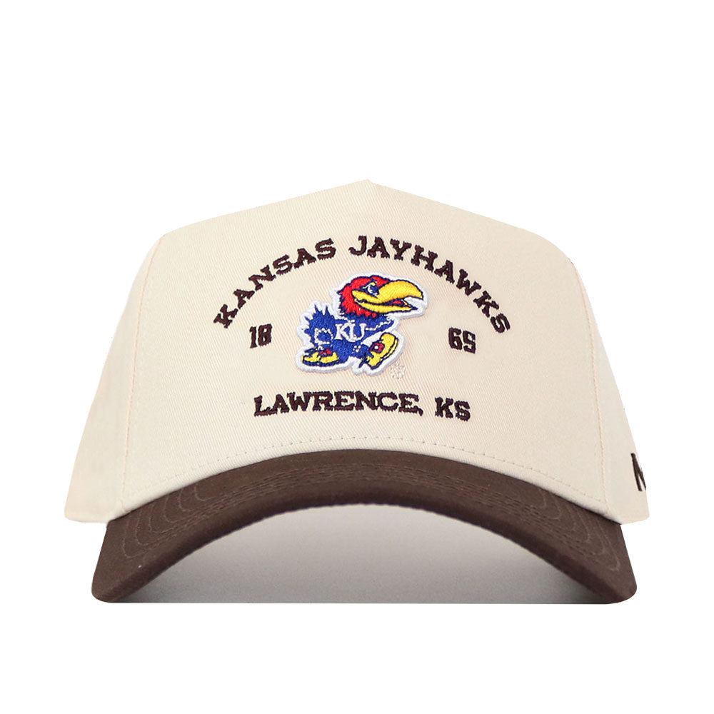 The Kansas Jayhawks Outlaw Hat - Classic by No Rivals is a beige cap with a brown brim, showcasing the Kansas Jayhawks logo along with "KANSAS JAYHAWKS," "1865," and "LAWRENCE, KS" embroidered on the front. Made from high-quality cotton and finished with detailed embroidered logos, this hat features a convenient snapback adjustment for a comfortable fit.