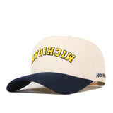 Introducing the Michigan Wolverines | Upside Down Michigan Hat - Classic by No Rivals—a beige and navy blue snapback cap made from premium cotton, showcasing “MICHIGAN” embroidered upside down in yellow across the front and a subtle “NO” logo on the side. This stylish cap blends comfort with a unique, eye-catching design.