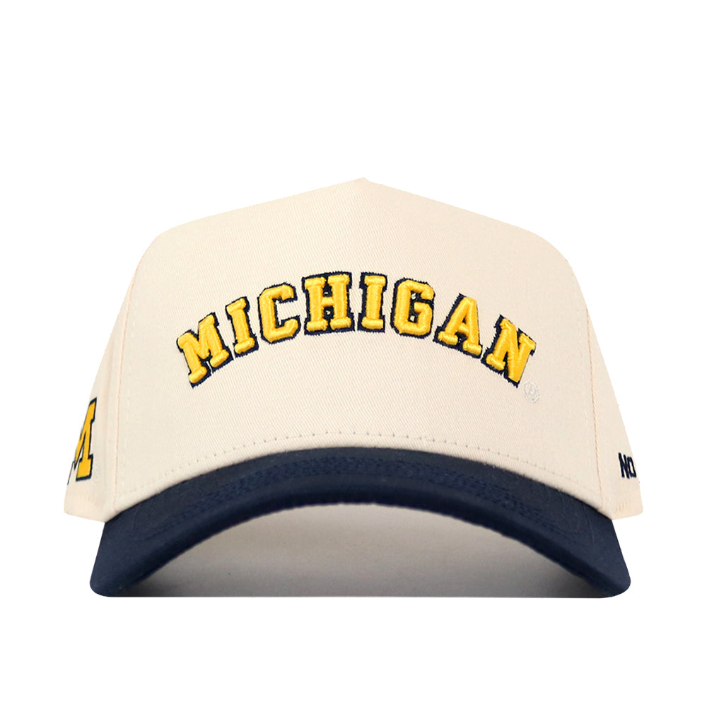 Show your Michigan pride with the No Rivals Right Side Up Michigan Hat - Classic Colors. This snapback features a cream crown, bold yellow “MICHIGAN” lettering outlined in black on the front, an embroidered logo detail, a dark blue brim, and is officially licensed for authentic team style.