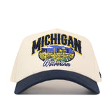 The No Rivals Michigan Wolverines Stadium Hat is a cream and navy snapback baseball cap featuring Michigan Wolverines text and an embroidered stadium scene on the front—perfect for completing your gameday fit.