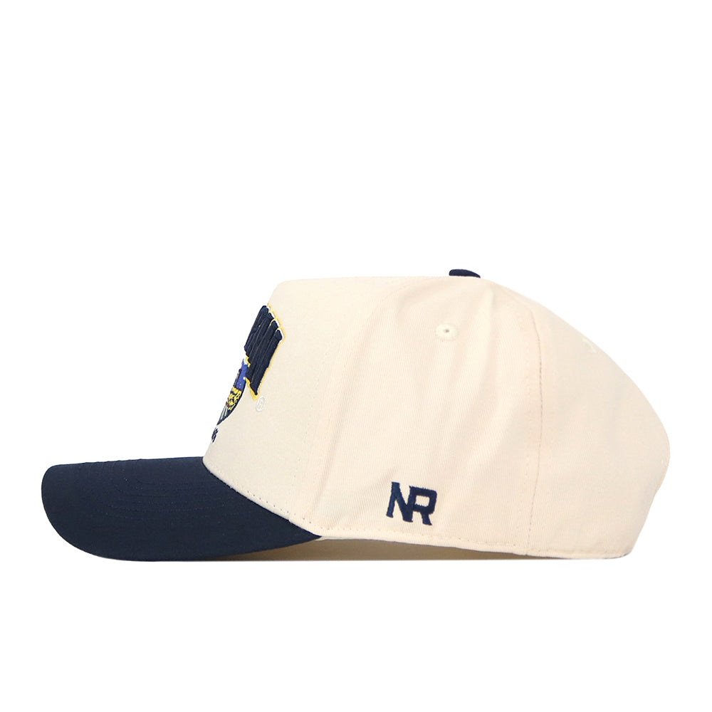 A beige Michigan Wolverines Stadium Hat by No Rivals, featuring a navy blue brim and side view. The initials NR are embroidered in navy blue on the side, adding a stylish logo that complements any gameday look.