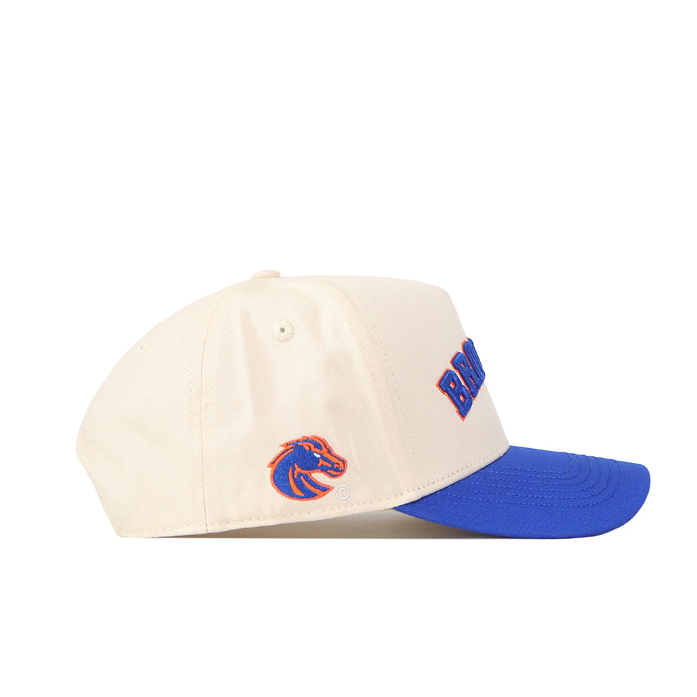 The Right Side Up Broncos Hat - Boise State - Classic by No Rivals is a cream-colored baseball cap with a blue brim, showcasing an officially licensed, embroidered Broncos logo on the front and a bronco head logo on the side. It features an adjustable snap back closure for a comfortable fit.
