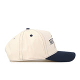 A side view of the No Rivals Michigan Wolverines Vintage Hat, featuring a beige crown with a navy blue brim and matching navy stitching. The front displays partially visible black text, while the classic snapback closure ensures an adjustable fit.
