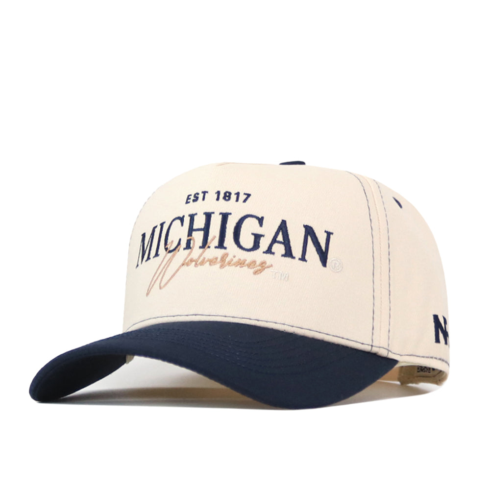 The No Rivals Michigan Wolverines Vintage Hat features a cream top with ventilation holes, a navy brim, and an officially licensed embroidered logo on the front displaying “MICHIGAN” and “Wolverines EST 1817.” This classic baseball cap includes a snap back closure for an adjustable fit.
