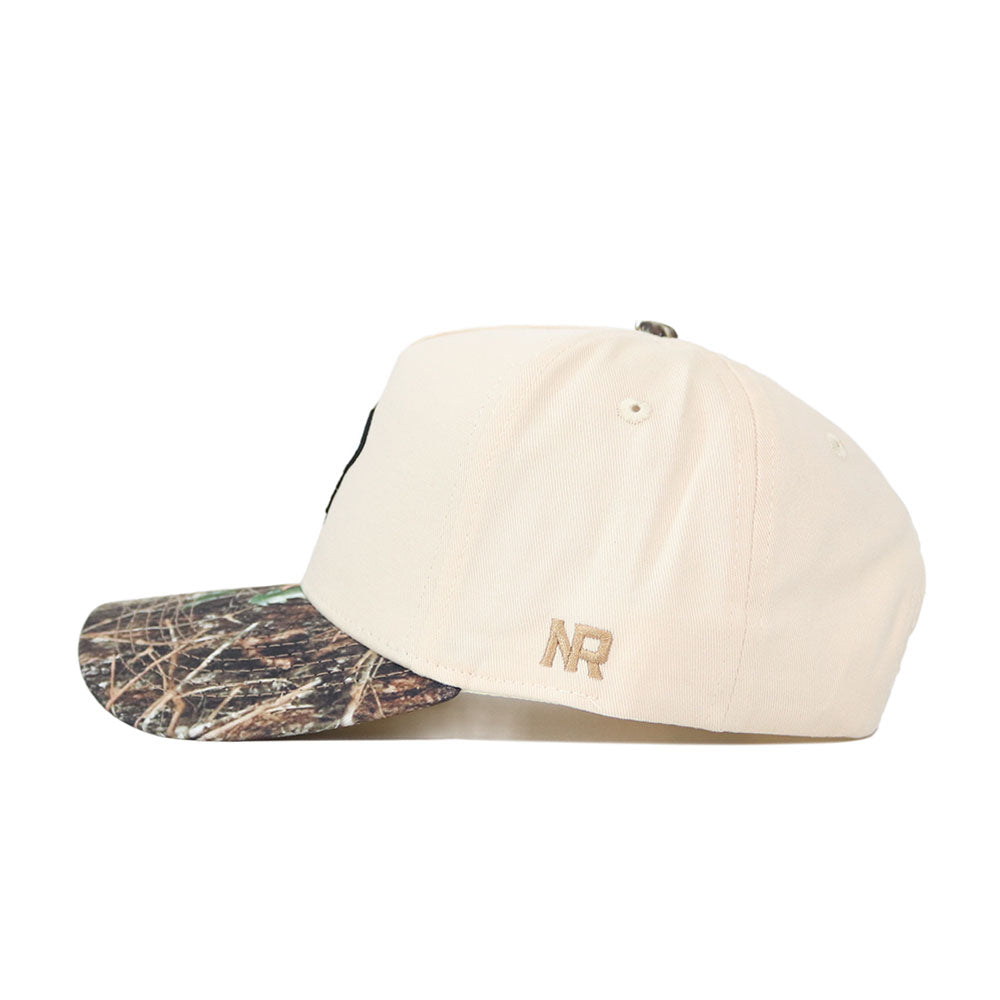 The OSU Pistol Pete Camo Hat - Connector Edition by No Rivals features a beige snapback with a camouflage brim and tan "NR" embroidery near the back, made from high-quality cotton and shown from the side.