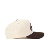 The Cowboys Script Espresso Hat by No Rivals is a cream-colored cotton baseball cap with a brown curved brim and brown embroidered text, shown from the side against a white background.