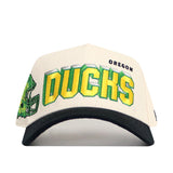 The No Rivals Oregon Alma Mater Hat is a white and black snapback with green and yellow "DUCKS" text, "OREGON" above it, embroidered logos, and a football helmet graphic on the left front.
