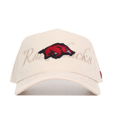 The No Rivals Arkansas Stacked Hat is a beige cotton baseball cap with an embroidered red razorback hog logo on the front and “Razorbacks” subtly stitched in beige behind the logo.
