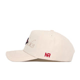 The Arkansas Stacked Hat by No Rivals is a beige snapback with red NR embroidery on the side and partially visible black and red cursive text on the front, crafted from high-quality cotton and shown on a white background.