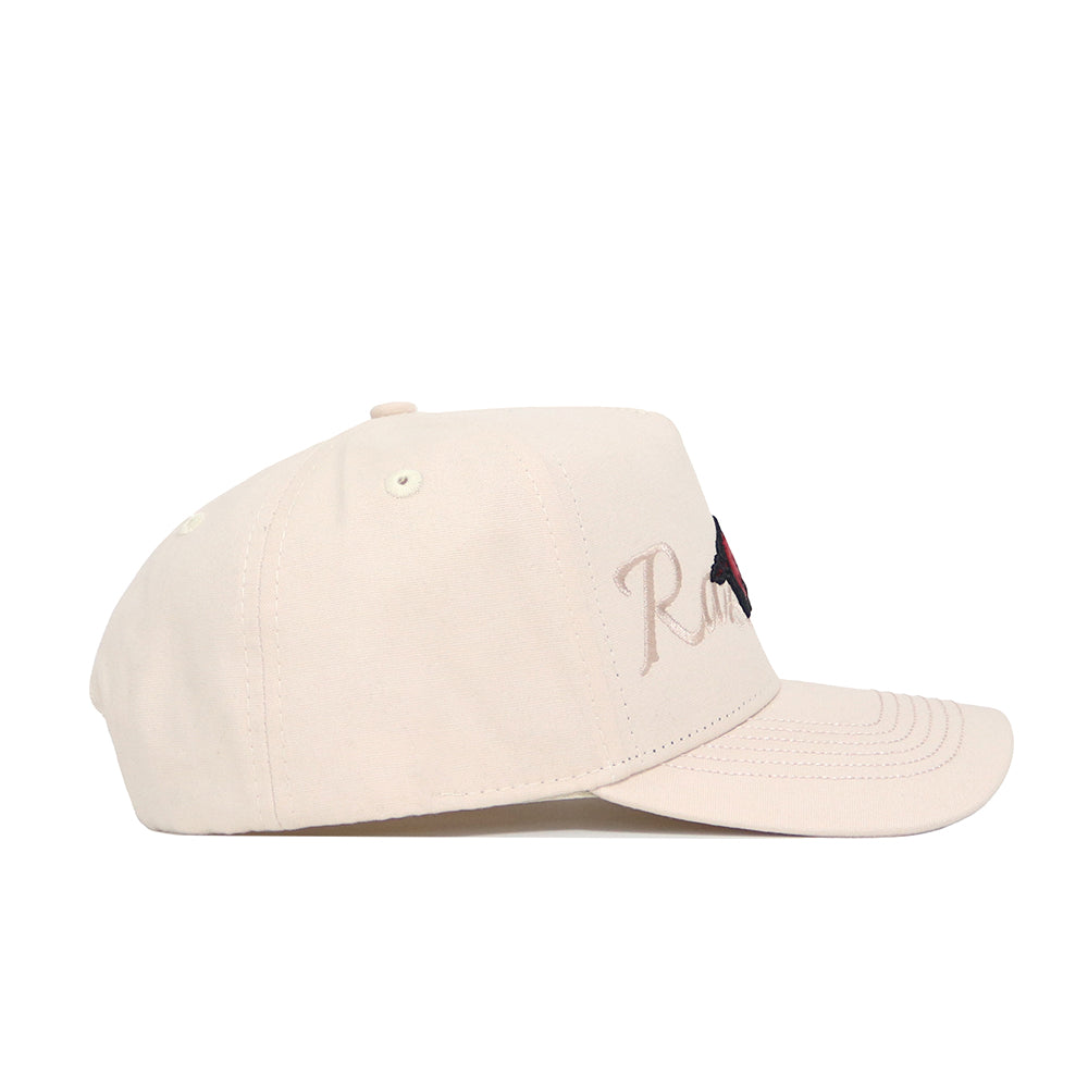 The Arkansas Stacked Hat by No Rivals is a beige cotton baseball cap with a curved brim, structured fit, and ventilation eyelets. It features embroidered text and a small front graphic, shown here from the side.