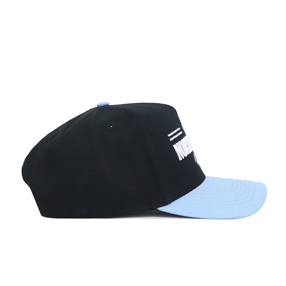 The No Rivals North Carolina Tailgate Hat is a black cotton snapback with a light blue brim and matching top button, shown from the side. It has a structured fit and partially visible white text and design on the front.
