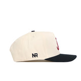 The Alabama Halftime Hat by No Rivals is a cream cotton baseball cap with a navy brim, featuring maroon embroidered J and NR logos and an adjustable snapback closure for a structured, comfortable fit.
