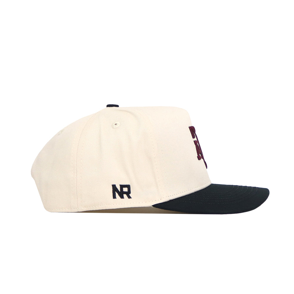 The Texas A&M Halftime Hat by No Rivals is a cream snapback with a black curved brim, featuring NR embroidery on the side. Made from quality cotton, it offers a structured fit, top ventilation eyelets, and a partially visible front design.