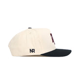The Texas A&M Halftime Hat by No Rivals is a cream snapback with a black curved brim, featuring NR embroidery on the side. Made from quality cotton, it offers a structured fit, top ventilation eyelets, and a partially visible front design.