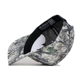 The Indiana Outland Hat by No Rivals is a high-quality cotton baseball cap featuring a woodland camo pattern in green, brown, and beige. Shown upside down, it reveals the inside label and black inner band.
