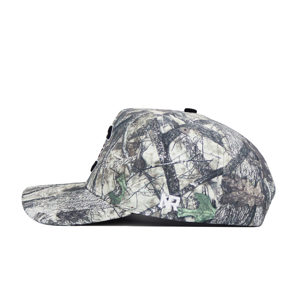 A side view of the South Carolina Outland Hat by No Rivals, a camo print cap with branches and leaves, flat brim, white embroidered NR logo near the back, structured fit, and adjustable snapback.
