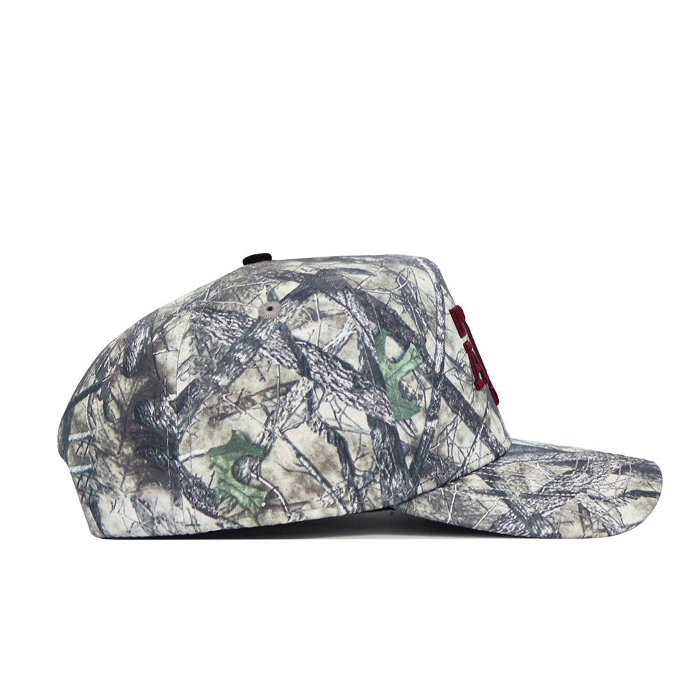 A side view of the No Rivals Texas A&M Outland Hat, a structured-fit, flat-brim snapback made from high-quality cotton with a natural branch and leaf camouflage pattern, displayed on a white background.