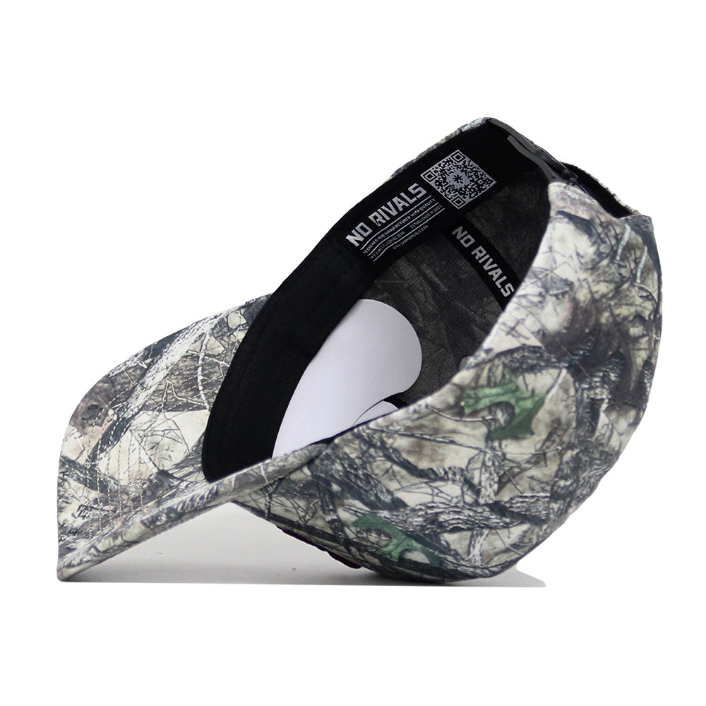 An upside-down Texas A&M Outland Hat by No Rivals reveals its black inner sweatband labeled "NO RIVALS" and a QR code on the rim. This structured snapback, made from high-quality cotton with a camouflage print, sits on a white surface.