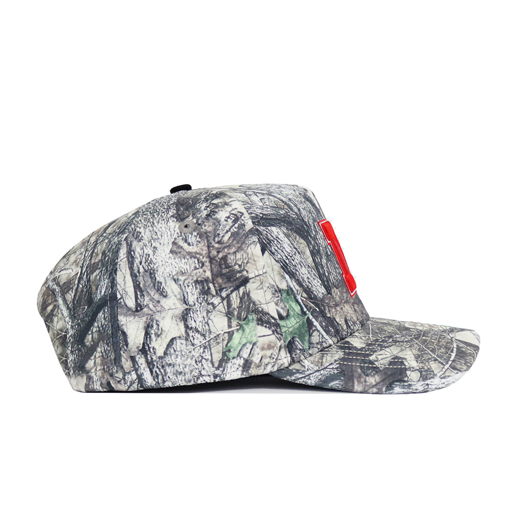 Side view of the Nebraska Outland Hat by No Rivals—a structured fit cap in camouflage with a flat brim and red rectangular front patch, made from high quality cotton, shown on a white background.