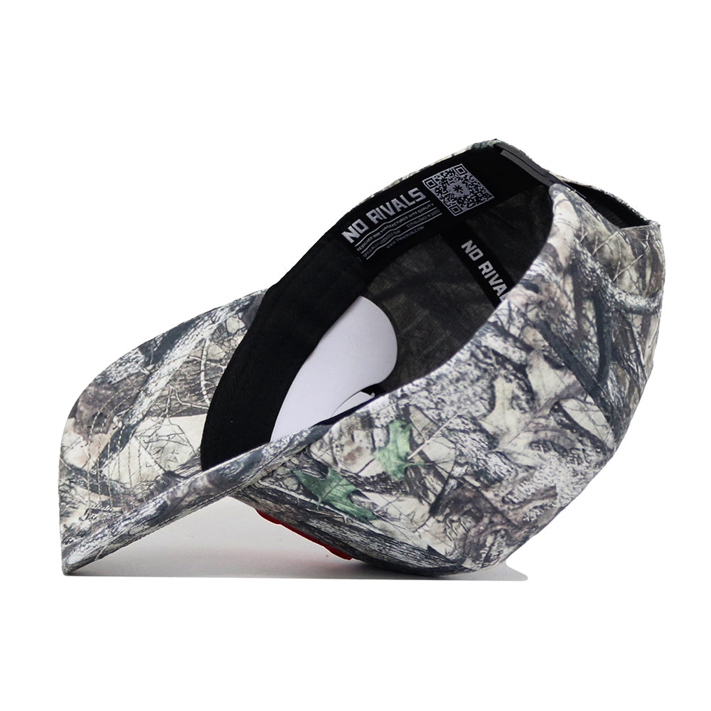 The Nebraska Outland Hat by No Rivals is displayed upside down on a white background, revealing its black inner band and the "NO RIVALS" print inside. This high-quality cotton cap features a bold camouflage pattern.