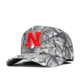 The No Rivals Nebraska Outland Hat is a structured cotton snapback with a woodland camo pattern, curved brim, and bold red "N" outlined in white on the front—perfect for Nebraska Cornhuskers fans.