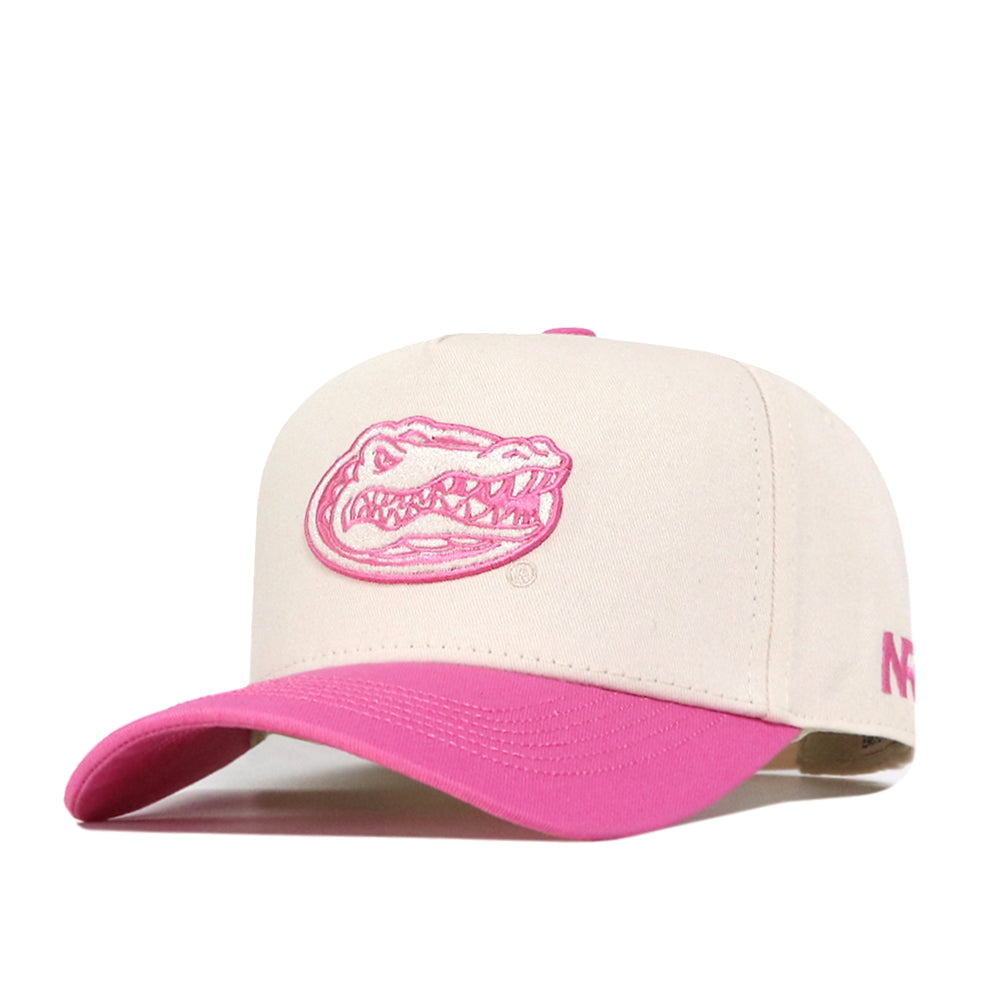 The Florida Pink Out Hat by No Rivals is a beige baseball cap featuring a pink brim and a pink embroidered alligator head logo on the front, with pink embroidered text on the side. This officially licensed snapback hat is a stylish way to show support as a breast cancer hat.