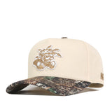 The Wichita State Camo Connector Hat by No Rivals is a beige cotton baseball cap with an embroidered palm tree logo on the front and a camouflage-patterned brim.