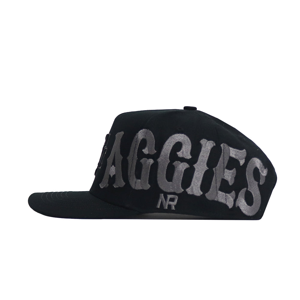 The Texas A&M Night Mode Hat by No Rivals is a black structured fit cap with a flat bill, featuring large gray "AGGIES" embroidery and small NR initials below.