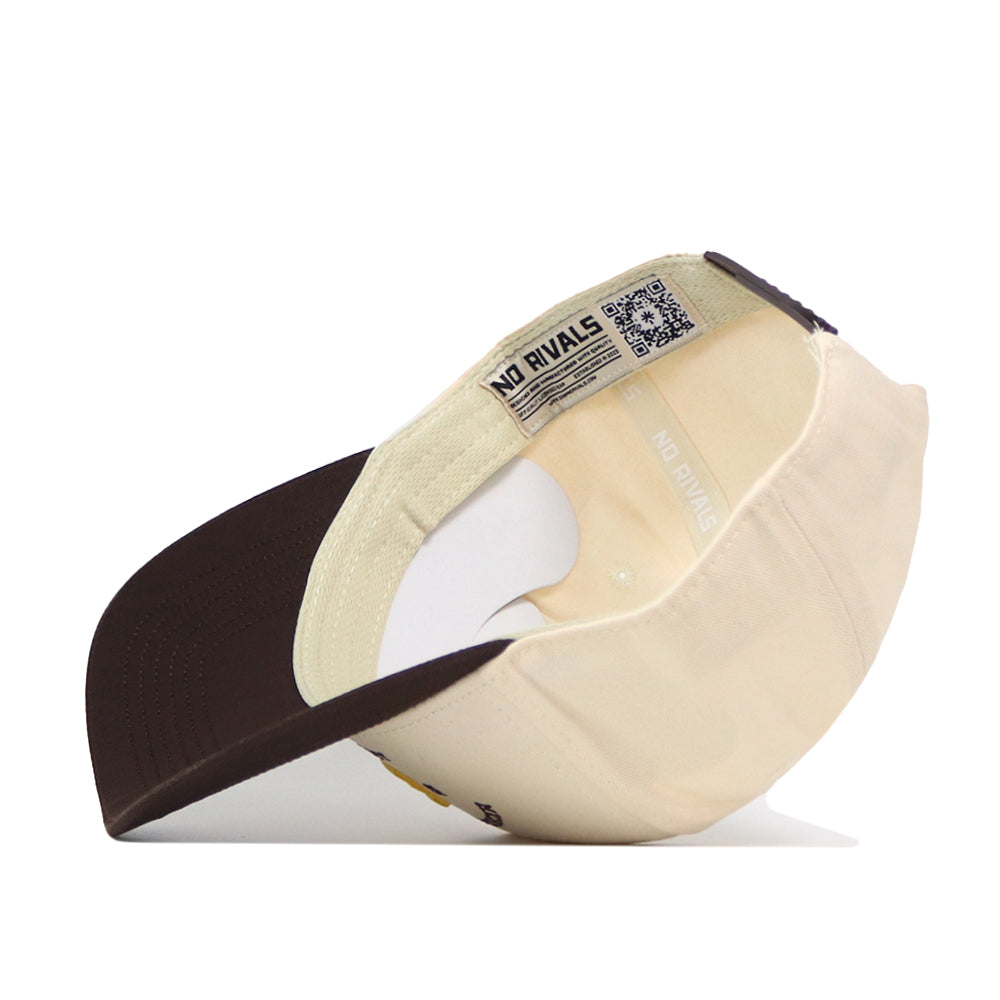 The Michigan Wolverines Outlaw Hat - Classic by No Rivals is displayed upside down, showcasing the inside label that reads “NO RIVALS” and a QR code on the inner tag. This beige and brown baseball cap features a brown brim and a classic snap back design for an adjustable fit—perfect for your gameday look.