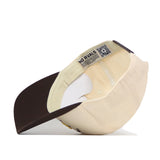 The Michigan Wolverines Outlaw Hat - Classic by No Rivals is displayed upside down, showcasing the inside label that reads “NO RIVALS” and a QR code on the inner tag. This beige and brown baseball cap features a brown brim and a classic snap back design for an adjustable fit—perfect for your gameday look.