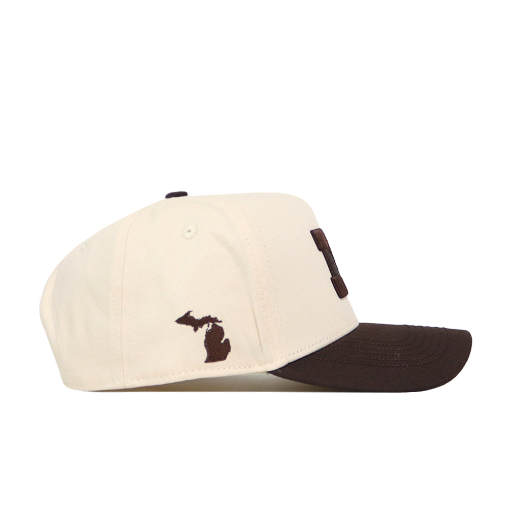 Introducing the Michigan Wolverines Espresso Hat by No Rivals—a cream-colored baseball cap accented with a brown brim and an embroidered outline of Michigan state in brown on the side. This stylish snapback is officially licensed to guarantee authenticity and quality.