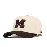 Introducing the Michigan Wolverines Espresso Hat by No Rivals—a cream-colored baseball cap featuring a prominent dark brown embroidered “M” on the front and a coordinated brown curved brim. The cap is finished with a small NR logo on the side and an adjustable snapback closure for a customized fit.