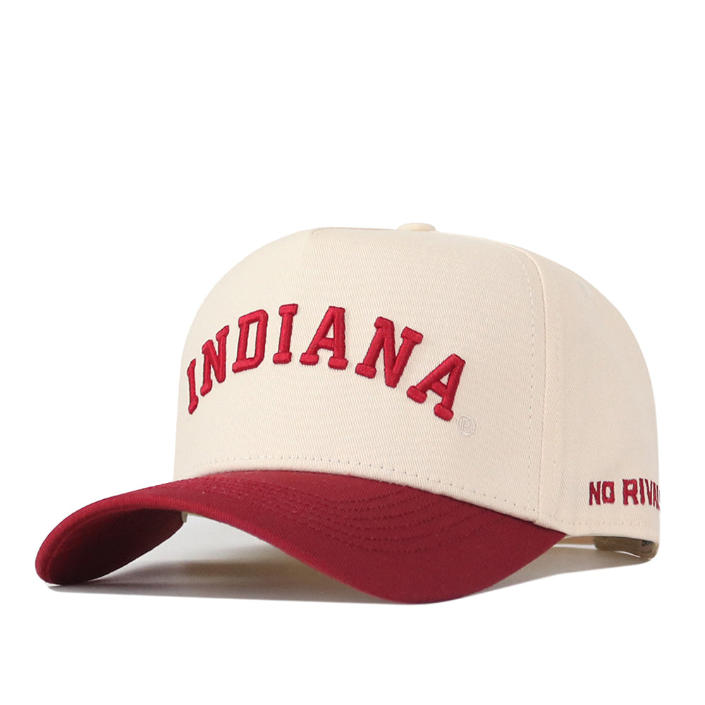 The Right Side Up Indiana Hat - Classic Colors by No Rivals is a cream-colored baseball cap made from high-quality cotton. It features “INDIANA” embroidered in red on the front and “NO RIVAL” stitched in red on the side of the red brim, with an adjustable snap back closure for a perfect fit.