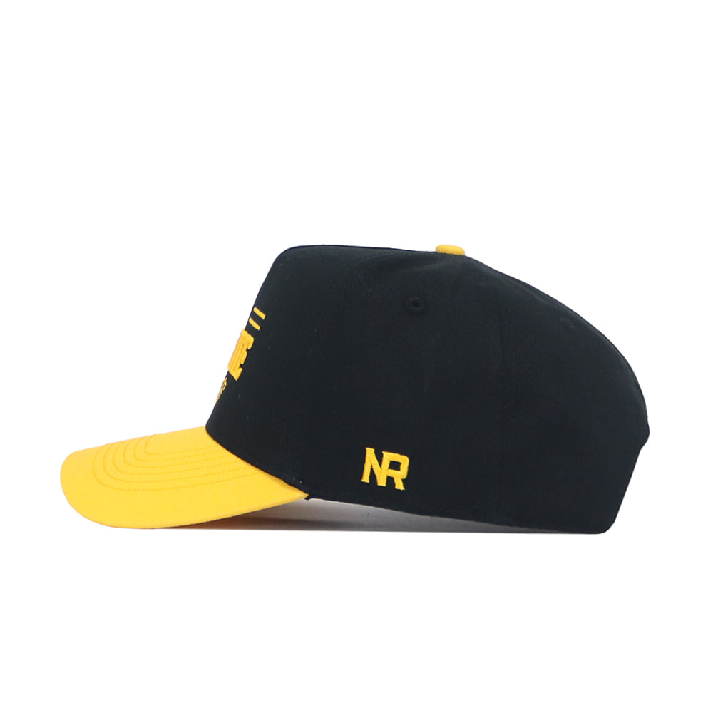 The No Rivals App State Tailgate Hat - 2 features a black snapback design with a yellow brim, yellow top button, and embroidered NR initials on the side—ideal for your game day look. Shown in side profile against a white background.