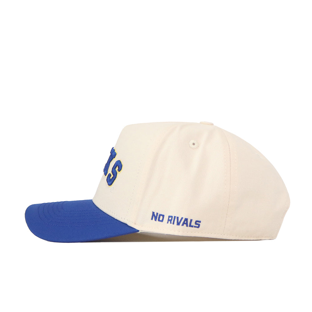 The Right Side Up Jacks Hat - Classic by No Rivals is a cream baseball cap with a blue brim, showcasing partially visible blue and yellow lettering on the front. The words “NO RIVALS” are embroidered in blue on the side, while an adjustable snapback closure ensures a comfortable fit. Representing the South Dakota State Jackrabbits, this hat blends classic style with modern comfort.
