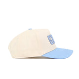 The No Rivals GTHD Hat, a cream-colored snapback with a light blue brim and embroidered front logos featuring partially visible blue letters, is displayed in side profile against a white background.