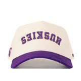 The No Rivals Washington Huskies Upside Down Huskies Hat - Classic is a white and purple snapback baseball cap, featuring an inverted “HUSKIES” logo embroidered in purple on the front.