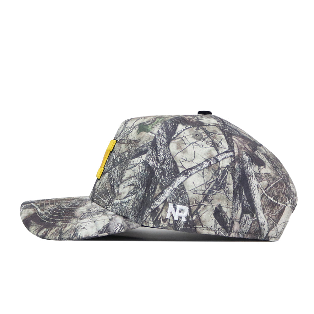 A side view of the Michigan Wolverines Outland Hat by No Rivals, a camouflage baseball cap with a yellow rectangle on the front, “NR” white embroidered letters on the side, and a Snap Back Adjustment for a comfortable Gameday Fit, shown against a plain white background.