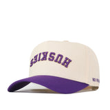 Introducing the Washington Huskies Upside Down Huskies Hat - Classic by No Rivals: a beige snapback hat featuring a purple brim and an inverted logo, with “HUSKIES” embroidered upside down in purple and gold on the front. The side of the brim is stitched with “NO RIVALS” in purple.