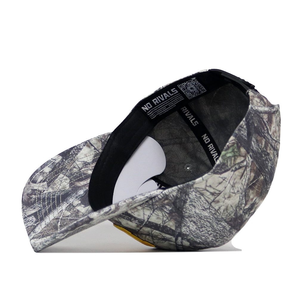 A Michigan Wolverines Outland Hat by No Rivals, featuring a camouflage snapback design, is shown upside down to display the interior black sweatband labeled “NO RIVALS” and white support material inside the crown.