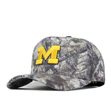 The No Rivals Michigan Wolverines Outland Hat is a camouflage baseball cap featuring a large, officially licensed yellow M embroidered on the front and a small ’47 logo on the side.