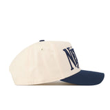 A cream-colored Nevada Wolf Pack Stride Hat by No Rivals is shown in profile, crafted from high quality cotton. This snapback cap features a navy blue brim and large, partially visible embroidered N and A in navy font on the front.