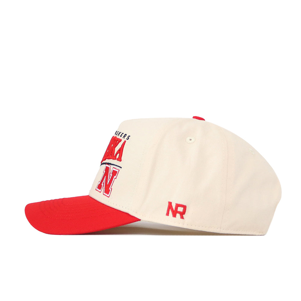 Introducing the Nebraska Cornhuskers Stride Hat by No Rivals: an officially licensed cream and red baseball cap featuring embroidered Nebraska and a large N on the front, with NR on the side. The cap is finished with a red brim and button.