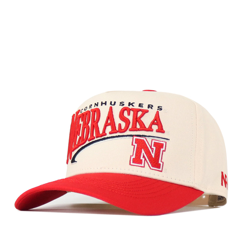 The No Rivals Nebraska Cornhuskers Stride Hat is an officially licensed white and red baseball cap featuring “NEBRASKA” and a bold red “N” embroidered on the front, accented with classic embroidered logos and a red bill. It also includes a convenient snap back closure for an adjustable fit.