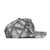 Side view of the No Rivals University of Florida Outland Hat, a structured fit snapback with a camouflage pattern and multicolored circular logo on the front; background shows tree branches and leaves.