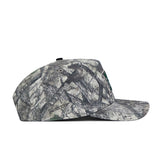 A side view of the No Rivals Hawaii Outland Hat, a flat-brim snapback featuring a camouflage pattern in grey, green, and brown tones resembling tree branches and leaves.