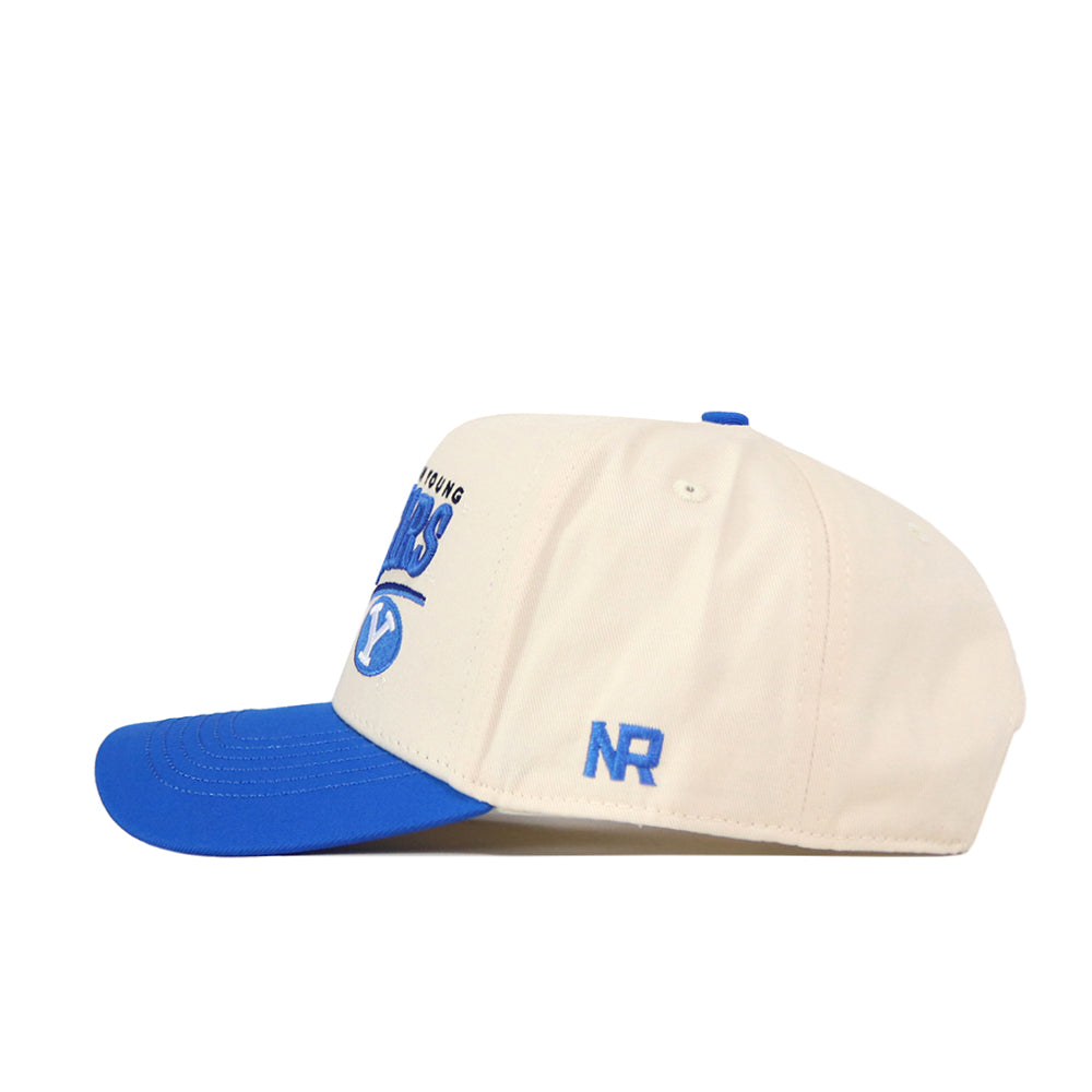 Show off your standout gameday style with the No Rivals BYU Cougars Stride Hat—a cream-colored snapback featuring a blue bill, blue top button, and embroidered blue ‘NR’ initials on the side. Bold BYU text and graphics in blue are partially visible on the front, making this cap a must-have for any fan.