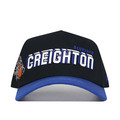 The Creighton Courtside Hat is an officially licensed snapback made from high-quality cotton, with CREIGHTON BLUEJAYS in white and blue on the front and a small basketball net graphic on the side.